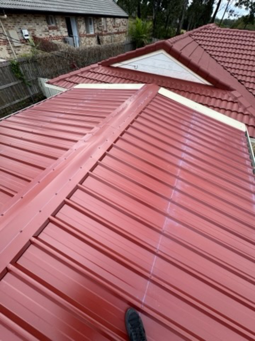 New red metal roof sheeting beside an existing tiled roof